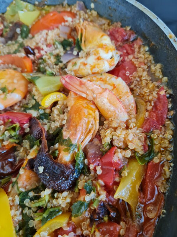 Close-up of a colorful traditional seafood dish in a pan, with prawns, vegetables, quinoa, and herbs, representing healthy and authentic Cretan cuisine.
